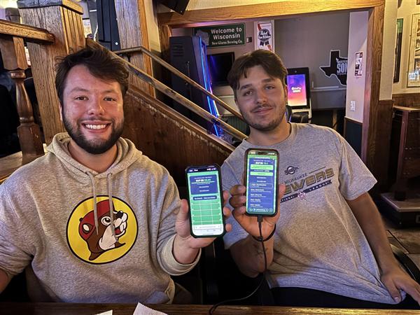 Two friends at Club 400 holding up their phones showing live Fantasy Draught scores