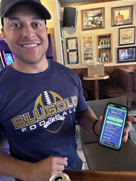 A smiling guest at Club 400 holding up his phone with his live Fantasy Draught score and an unlocked reward