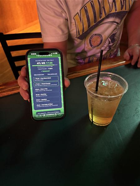 A guest's phone showing a redeemed reward next to a drink on the table at Club 400